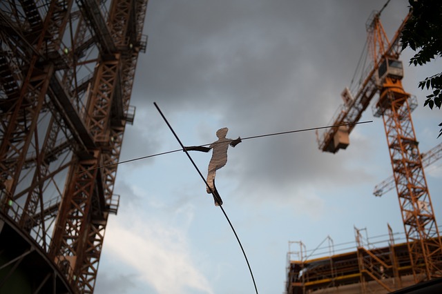 An image depicting a skilled tightrope walker gracefully navigating a high wire, balancing between towering stacks of money on one side, and a deep, treacherous pit on the other