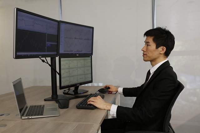 An image showing a focused trader sitting in front of multiple computer screens, displaying real-time charts and data