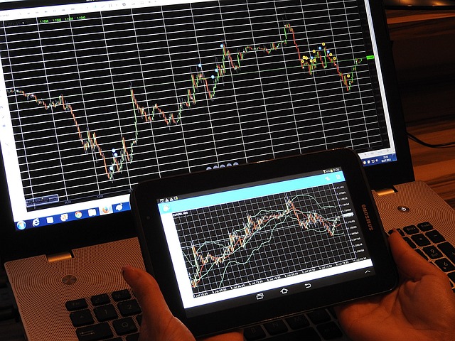 An image featuring a person sitting at a desk with multiple computer screens displaying real-time forex charts and Questrade's trading platform